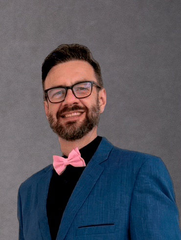Prof. Marcos Paulo Montanhani, perito judicial matemático, sorrindo, de terno azul e gravata borboleta rosa
